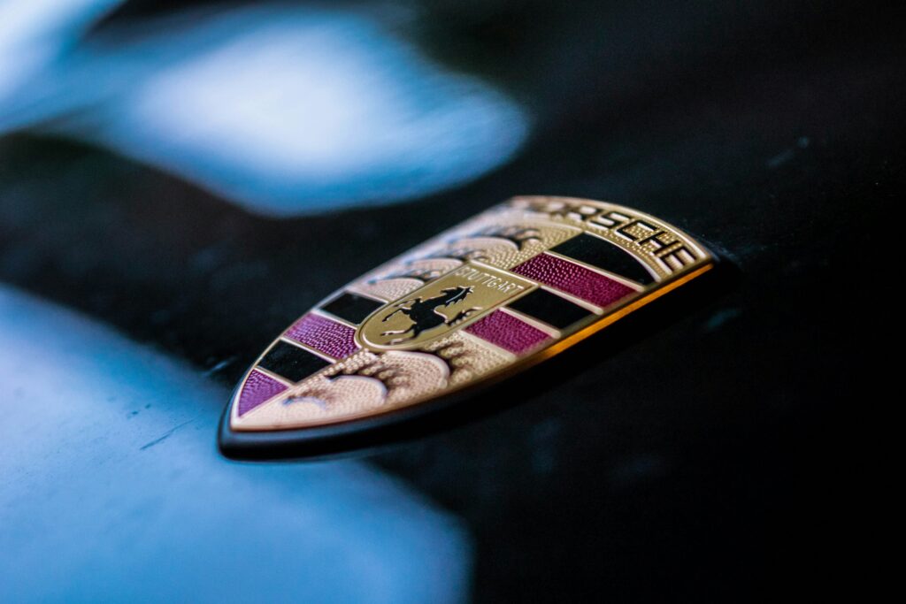 Close-up of a Porsche emblem on a black car hood with metallic reflections.